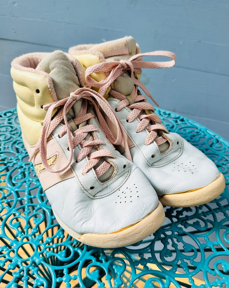 May include: A pair of pastel-coloured high-top trainers with pink laces. The shoes are made of leather and have a white sole.