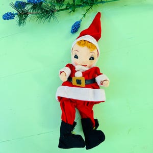 Peut inclure: Une poupée vintage de Père Noël avec une combinaison rouge, des bordures blanches et des bottes noires. La poupée a un visage peint avec des cheveux blonds et porte une ceinture noire avec une boucle dorée.