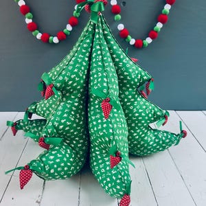 以下が含まれることがあります： 赤と白のポンポンと緑と白のガーランドが付いた緑の布製のクリスマスツリー