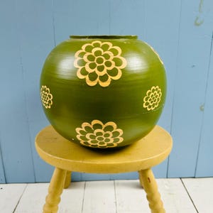 Peut inclure: Un vase sphérique vert olive orné d'un motif répétitif de fleurs stylisées beige clair. Le vase présente un corps lisse et arrondi avec une large ouverture sur le dessus, mettant en valeur un design floral cohérent sur toute sa surface.