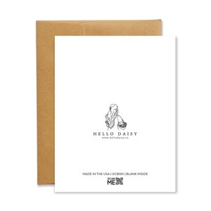 The back of the Hello Daisy greeting card. Features the Hello Daisy logo: a girl with long hair holding a basket of daisies. Below the logo is the text: Made in the USA, the SKU number, Blank inside, as well as a Scan Me QR code.