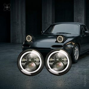 Peut inclure: Deux phares LED ronds avec des boîtiers noirs et des anneaux halo circulaires blanc brillant. Les lumières présentent une lentille de projecteur centrale et des réflecteurs latéraux. Ces pièces automobiles sont devant une voiture de sport noire.