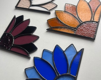Könnte beinhalten: Vier Eckscheiben aus Buntglas in Form einer Sonnenblume. Die Scheiben sind in den Farben Weiß, Orange, Burgunderrot und Blau.