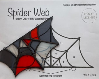 May include: A stained glass spider web pattern with black, grey, white, and red glass pieces. The pattern is 9 inches by 4.5 inches and includes a suggested ring placement.
