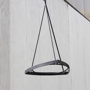 May include: A black metal hanging planter with a triangular frame and a circular base. The planter is suspended from a hook attached to a horizontal bar, ideal for displaying plants. The design is minimalist and modern.