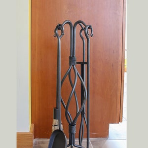 May include: A black metal fireplace tool stand with a twisted design. The stand holds a broom, poker, and shovel.