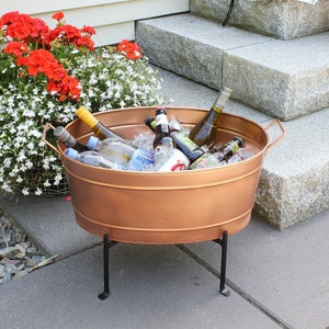 May include: A copper cooler with a black metal stand filled with ice and various bottles of beer and wine. The cooler is sitting on a set of stone steps.