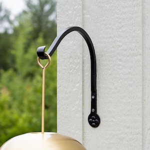 May include: Black metal hanging bracket with a curved arm and decorative rivets. A gold-colored metal ring and rod support a gold-colored, semi-circular shade, likely for a bird feeder or outdoor light fixture.
