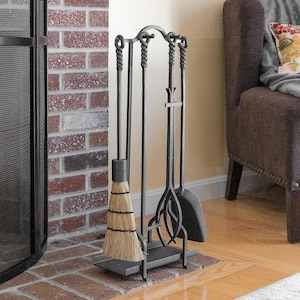May include: A black fireplace tool set with a broom, poker, shovel, and stand. The tools have twisted handles and are arranged on a rectangular base. The broom has a natural fiber head. The set is placed on a brick hearth.