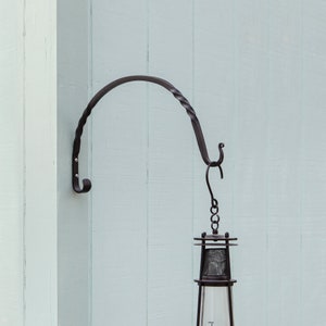 May include: Black metal hook mounted on a light blue wall with a black metal lantern hanging from it.