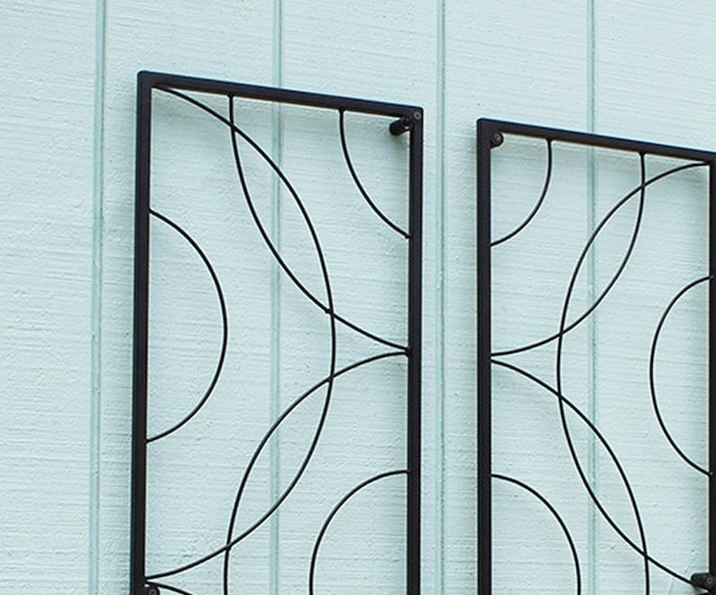 May include: Two black metal decorative wall panels with a geometric design of intersecting curved lines. The panels are rectangular and mounted on a light blue textured wall.