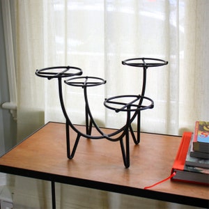 May include: A black metal plant stand with three tiers. The stand has a curved design and is made of thin metal rods. The stand is sitting on a wooden table.
