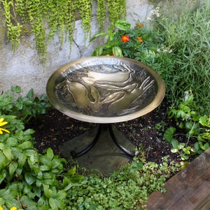 May include: A brass bird bath with a raised design of hares and a circular base. The bird bath is on a black metal stand with three legs.