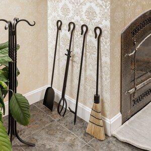 May include: A black fireplace tool set with a shovel, tongs, poker, and broom. The tools are arranged against a patterned wall near a fireplace. The set includes a stand with a twisted design and a plant.