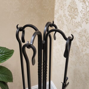 May include: A black wrought iron fireplace tool set. The set includes a poker, shovel, and brush, all with decorative curved handles. The tools are displayed in a matching stand with a scrolled design, perfect for keeping a hearth tidy and stylish.