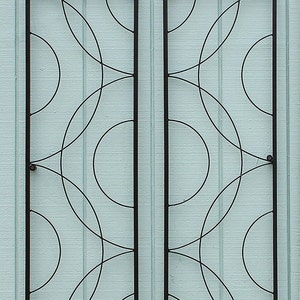 May include: Two rectangular, black metal wall art pieces with a repeating pattern of overlapping circles. The art is mounted on a light blue, vertically-paneled wall. The design is modern and geometric.