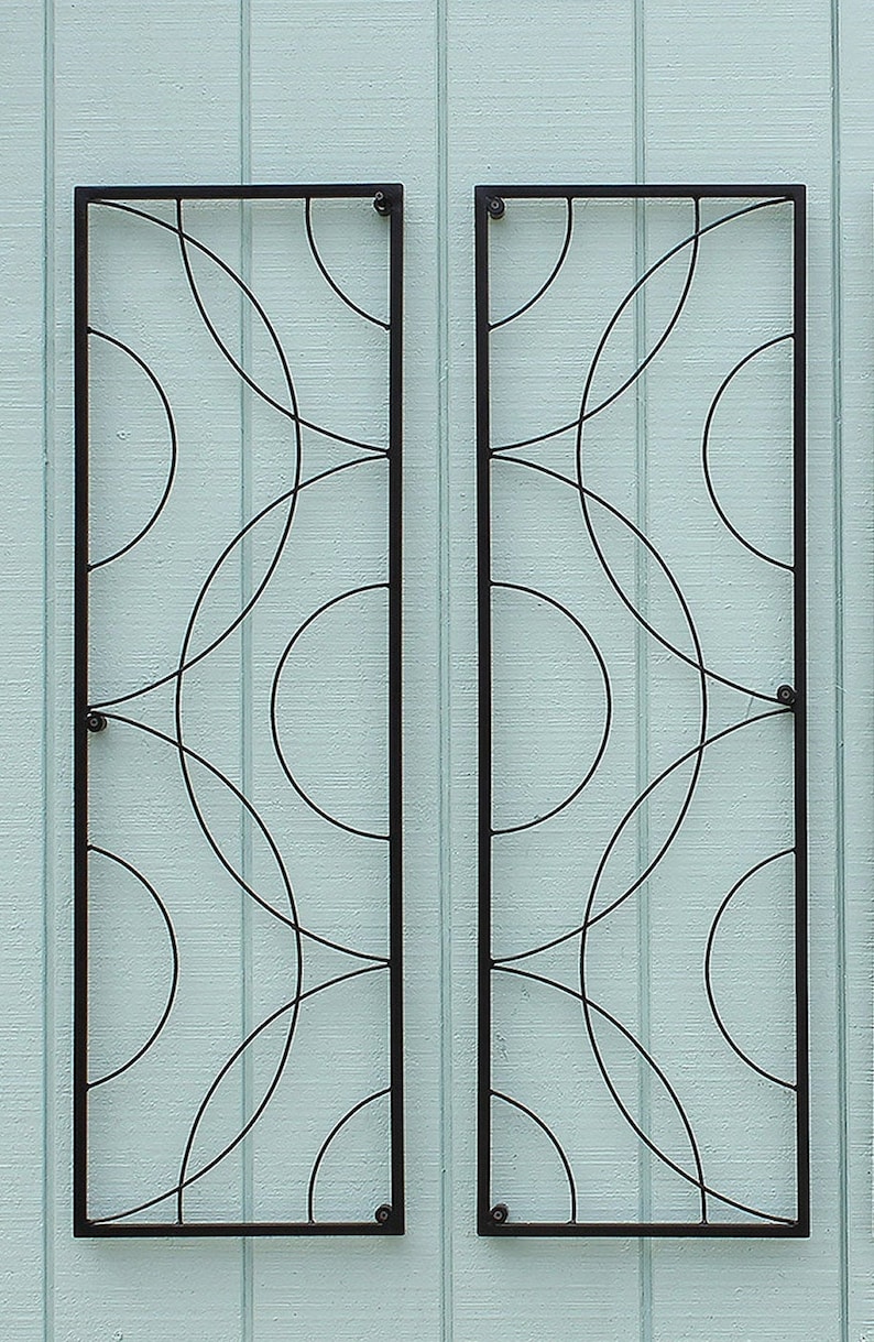 May include: Two rectangular, black metal wall art pieces with a repeating pattern of overlapping circles. The art is mounted on a light blue, vertically-paneled wall. The design is modern and geometric.