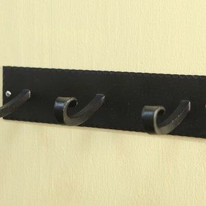 May include: Black metal wall mounted coat rack with three hooks. The hooks are curved and have a decorative design.