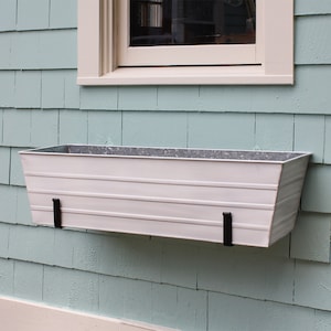 May include: White metal planter box with black metal brackets mounted on a light blue wall. The planter is designed to be hung on a wall.