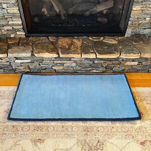 May include: A light blue rug with a dark blue border. The rug is placed in front of a stone fireplace.