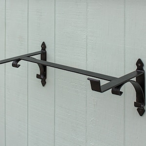 May include: Black metal wall-mounted shelf with two hooks. The shelf has a decorative scroll design on the brackets.