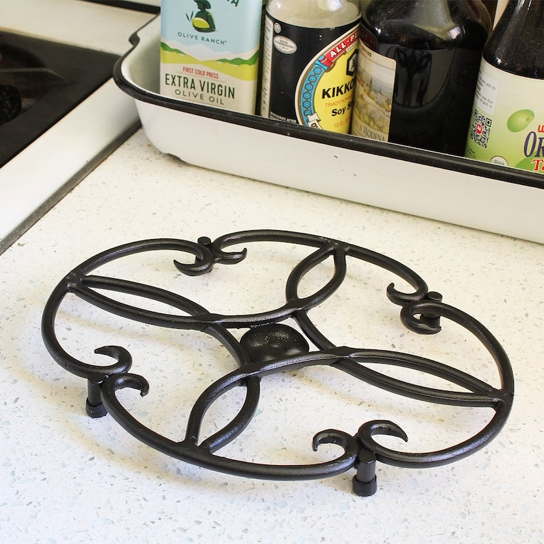 Op de afbeelding: Een ronde zwarte metalen onderzetter met een decoratief ontwerp. De onderzetter is rond en heeft een verhoogd midden.