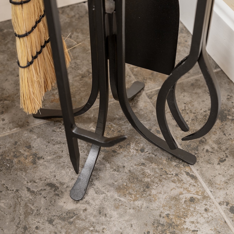 May include: A black fireplace tool set with a matching stand. The set includes a poker, shovel, and brush. The stand has a decorative, curved design. A natural-colored broom is attached to the stand.