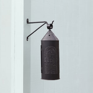 May include: A black metal lantern with a decorative design hangs from a black metal bracket mounted on a light blue wall. The lantern has a conical top and a cylindrical body with a patterned design.