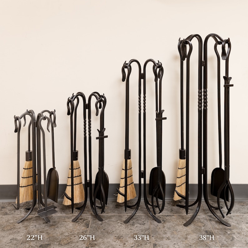 May include: A set of black wrought iron fireplace tools, including a broom, shovel, poker, and tongs. The tools are displayed in a stand, with heights ranging from 22 to 38 inches. The broom has a natural straw brush.