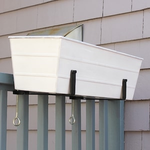 May include: White planter box with black metal brackets attached to a gray wooden railing. The planter box is hanging over the railing.