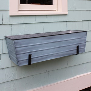Peut inclure: Une jardinière en métal bleu clair avec des supports en métal noir. La jardinière est fixée à l'extérieur d'une maison bleu clair.