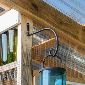 May include: A black metal hook mounted to a wooden beam, with a glass lantern hanging from it. The lantern has a blue glass shade and is surrounded by a wire mesh.