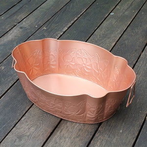 May include: A copper-colored metal planter with a scalloped rim and embossed floral design. The planter is oval-shaped and has two handles.