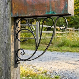 May include: A black metal mailbox bracket with a decorative leaf design. The bracket is mounted on a weathered wooden post and supports a copper-colored mailbox. The design features curved lines and leaf-shaped accents, adding a touch of elegance to the outdoor decor.