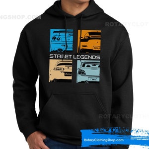 Może przedstawiać: Czarna bluza z kapturem z grafiką czterech różnych samochodów ułożonych w siatkę. Samochody to niebieski Nissan Skyline GT-R, żółty Mazda RX-7, żółty Toyota Supra i niebieski Subaru Impreza WRX. Pod samochodami nadrukowany jest tekst "STREET LEGENDS".
