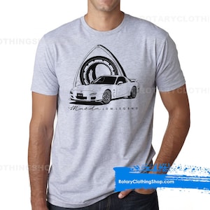 Könnte beinhalten: Ein graues T-Shirt mit einer Schwarzweiß-Illustration eines Mazda RX-7 Autos und eines Rotationsmotors. Der Text "Mazda JDM Legend" ist unter dem Auto aufgedruckt.