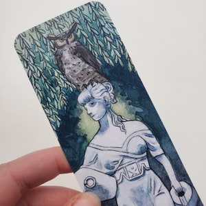 May include: A watercolor painting of a woman with an owl perched on her head. The woman is wearing a white dress and holding a shield. The background is a dark green forest with leaves.