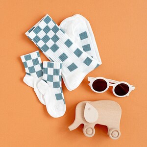 May include: A set of two pairs of white socks with a blue and white checkered pattern, a pair of white sunglasses, and a wooden toy elephant on a solid orange background.
