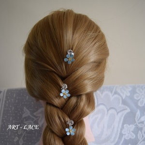 Puede incluir: Tres pinzas para el pelo con forma de flor azul con pedrería. Las pinzas están en el pelo castaño de una mujer.