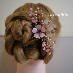 May include: A hair comb featuring delicate copper wire branches adorned with translucent pink and white flower petals, small white beads, and dark centers. The design includes the text ART-LACE. The floral arrangement is secured in a braided hairstyle.
