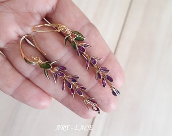 May include: A pair of gold dangle earrings with purple and green enamel flowers. The earrings are long and delicate, with a floral design.