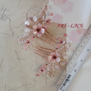 May include: Two hair combs featuring rose gold wire branches adorned with translucent pink and white flower petals and small white beads. A clear plastic ruler shows the combs measure approximately 4 inches in length. The text ART-LACE is visible.