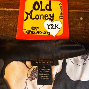 May include: A black and white floral print garment with a black collar. A tag reads "BCBGMAXAZRIA" and lists the material as 97% polyester and 3% spandex. A yellow and red sign with "Old Money" and "Y2K" is in the background.