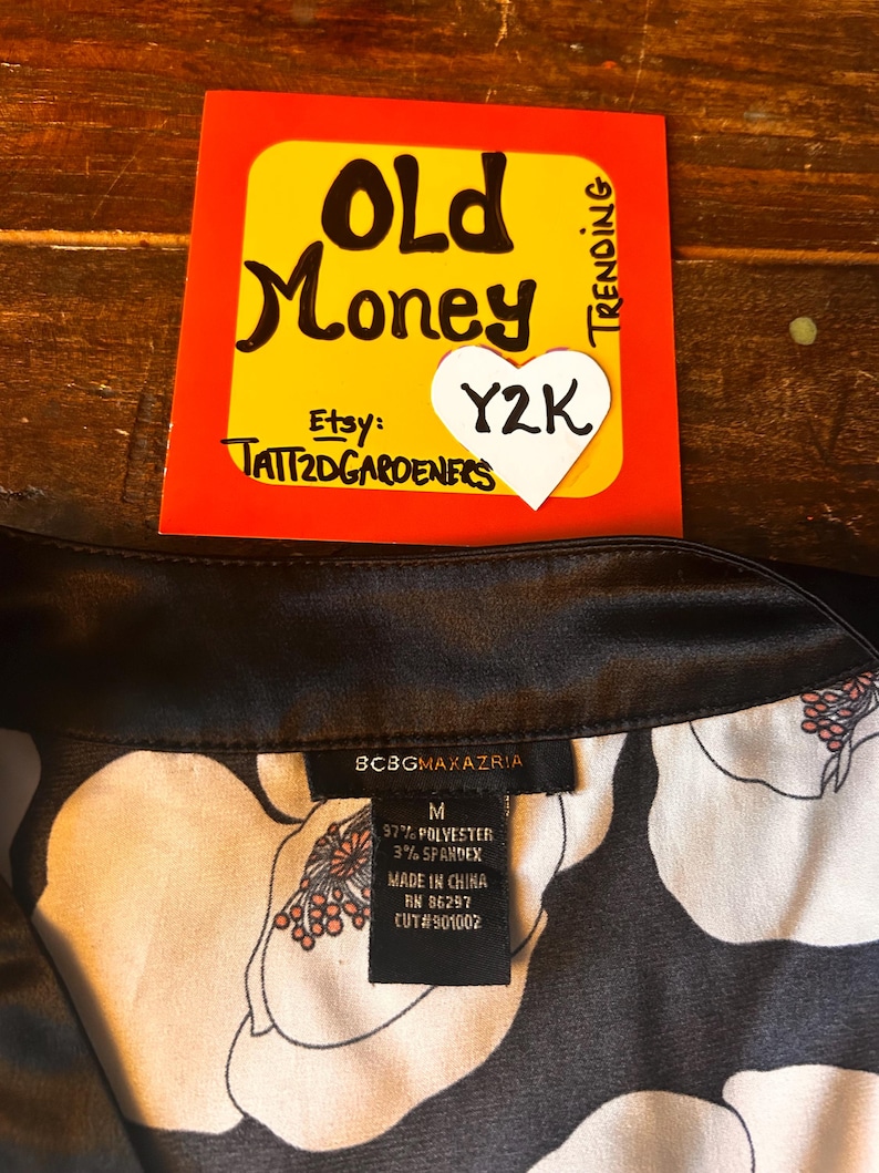 May include: A black and white floral print garment with a black collar. A tag reads "BCBGMAXAZRIA" and lists the material as 97% polyester and 3% spandex. A yellow and red sign with "Old Money" and "Y2K" is in the background.