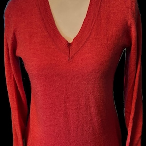 May include: A red V-neck sweater with long sleeves and button details on the cuffs. The sweater is displayed on a mannequin. A small sign at the bottom reads "Y2K trending" and "ETSY: TANZOCROMER".