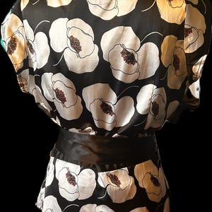 May include: Black and white floral print top with a black satin belt. The top features a large floral pattern with white petals and brown centers. The top has a black collar and the text "Old Money" on a small orange card.