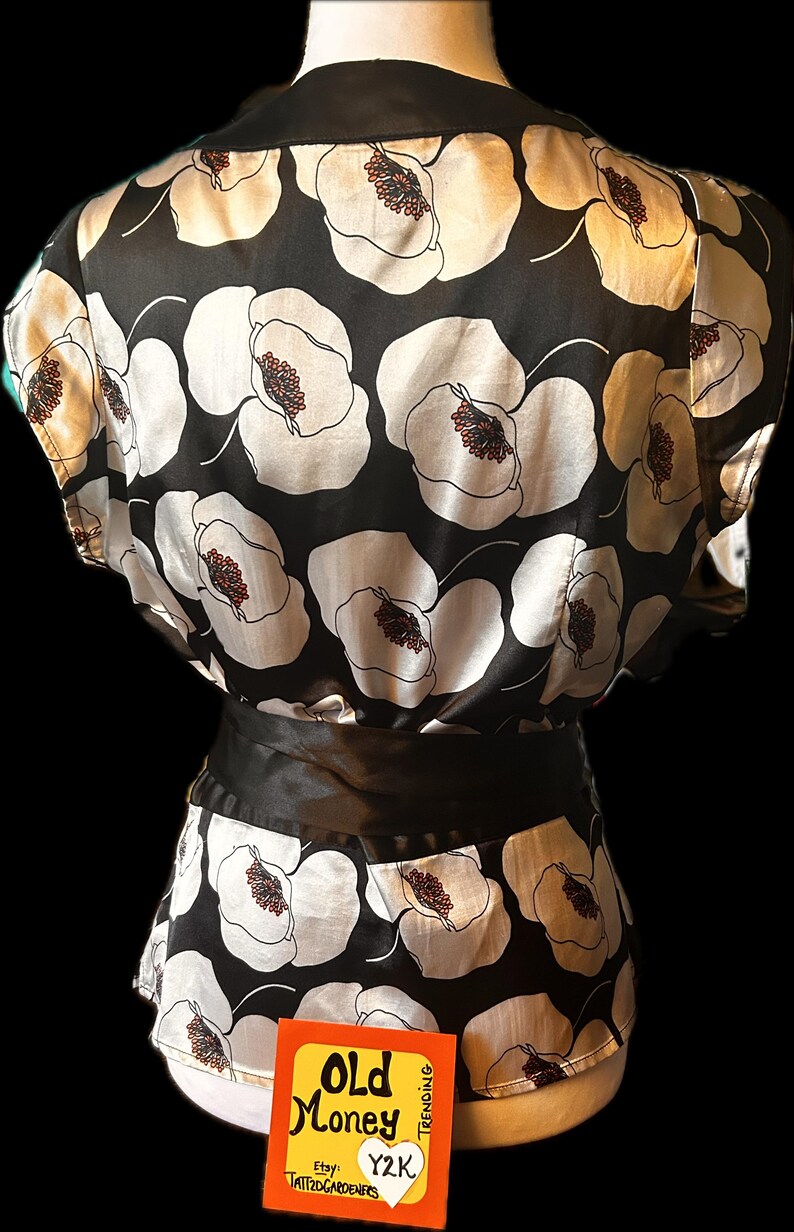 May include: Black and white floral print top with a black satin belt. The top features a large floral pattern with white petals and brown centers. The top has a black collar and the text "Old Money" on a small orange card.