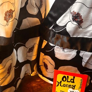 May include: Black and white floral print fabric with a satin finish. The design features large white flowers with orange and red centers against a black background. A tag with the words "Old Money" and "Y2K" is visible.