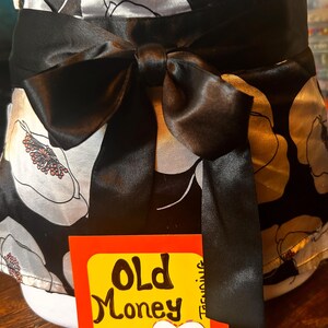 May include: A black and white floral print top with a large black bow at the waist. The top has a satin finish and a tag that reads "Old Money" and "Y2K" with the Etsy shop name.
