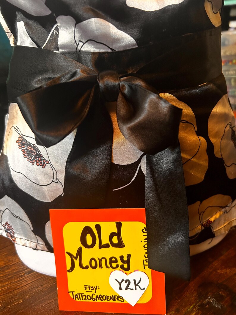May include: A black and white floral print top with a large black bow at the waist. The top has a satin finish and a tag that reads "Old Money" and "Y2K" with the Etsy shop name.